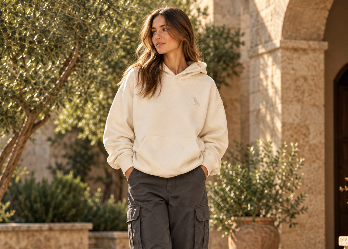 Woman in a bone raven hoodie and charcoal cargo pants in a sunlit stone courtyard